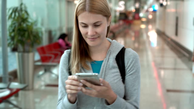 Frau-zu-Fuß-im-Flughafen-terminal.-Verwendung-von-Smartphone,-browsing,-messaging-mit-Freunden,-lesen-Nachrichten