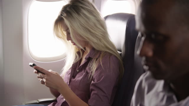Young-woman-using-mobile-phone-on-airplane-flight