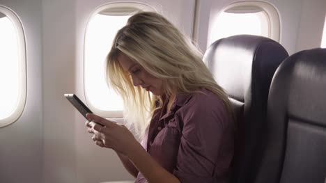 Mujer-joven-con-tableta-digital-en-el-vuelo-en-avión
