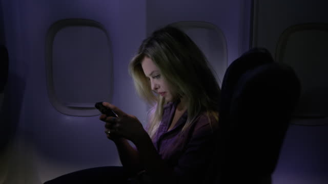 Woman-using-cell-phone-at-night-on-airplane