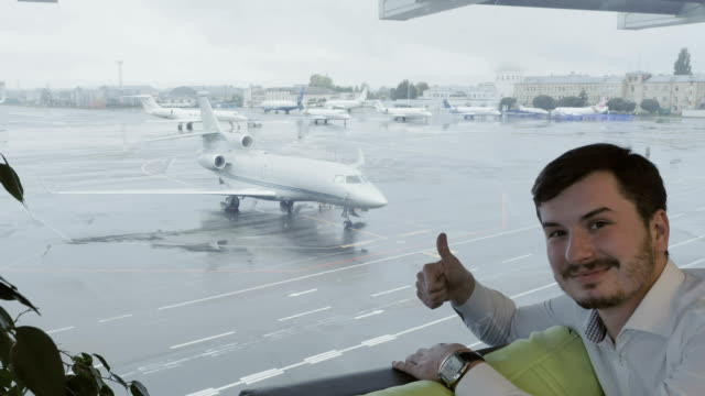 Nette-Mann-am-Flughafen-zeigt-der-Daumen-nach-oben-auf-die-Kamera