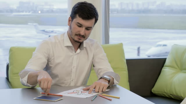Businessman-paints-coloring-book-while-waiting-boarding-on-plane-in-airport