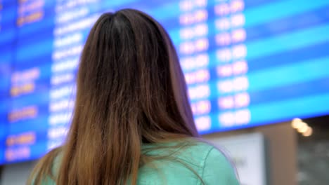 Mujer-joven-se-ve-en-el-tablero-de-información-de-las-salidas-en-el-aeropuerto.