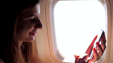 Eine-schöne-Frau-nutzt-das-Telefon,-an-das-Fenster-des-Flugzeugs-sitzen