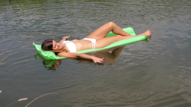 Junge-gebräunte-Frau-In-einem-weißen-Bikini-schwimmend-im-Fluss-auf-der-Matratze.