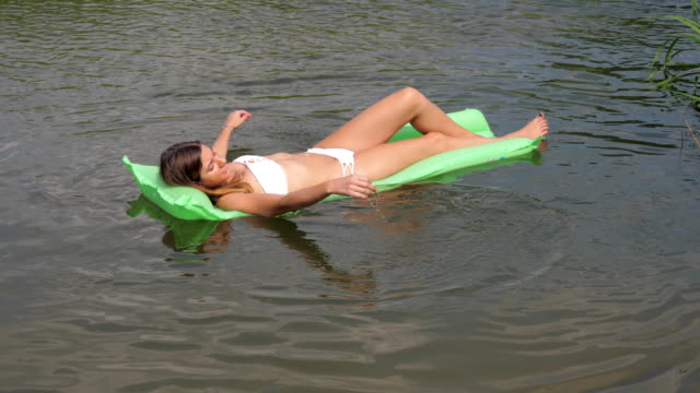 Junge-gebräunte-Frau-In-einem-weißen-Bikini-schwimmend-im-Fluss-auf-der-Matratze.
