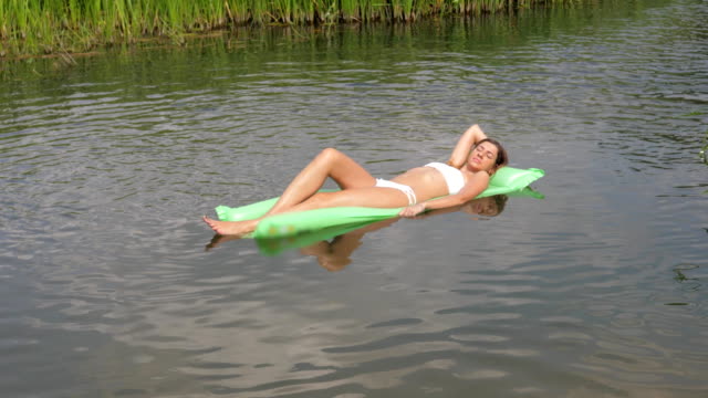 Pretty-Tanned-Woman-In-A-White-Bikini-Floating-In-The-River-On-The-Mattress.