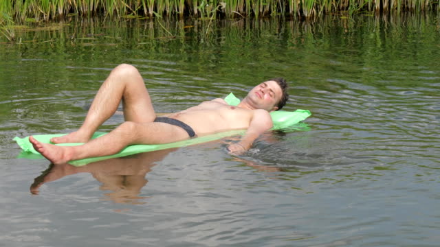 El-hombre-de-reclinación-en-el-caluroso-día-de-verano-de-natación-en-el-río-sobre-el-colchón.