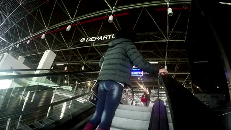Attractive-female-on-airport-departure-escalator-wave-hand-farewell