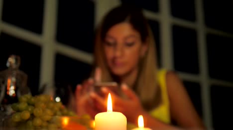 Frau-im-gelben-Kleid-mit-Abendessen-im-Restaurant-bei-Kerzenlicht-nutzt-Smartphone