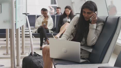 Mujer-hablando-por-teléfono-celular-usando-un-ordenador-portátil-en-el-aeropuerto