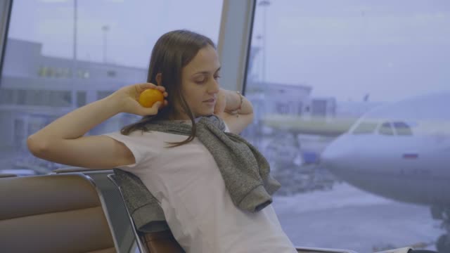 Young-woman-sits-and-stretches-at-airport-with-airplane-on-the-background