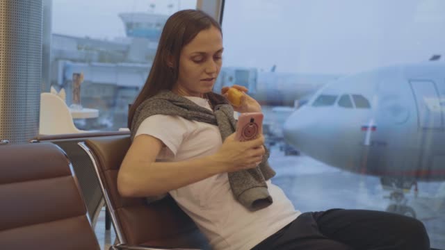 Young-woman-eats-tangerine-at-airport-with-airplane-on-the-background