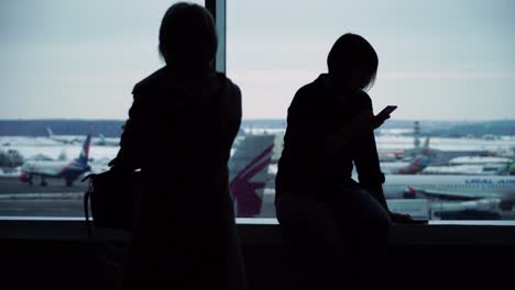 Frau-im-Flughafen-terminal-warten-auf-Flug-mit-smartphone
