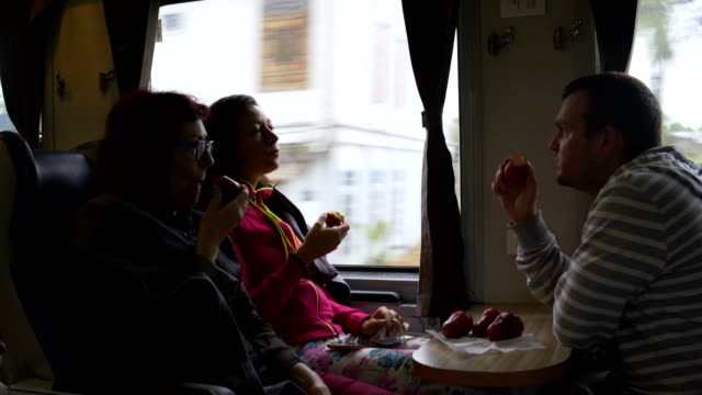 A-man-and-women-are-sitting-on-the-train,-eating-Malayan-apples-and-talking