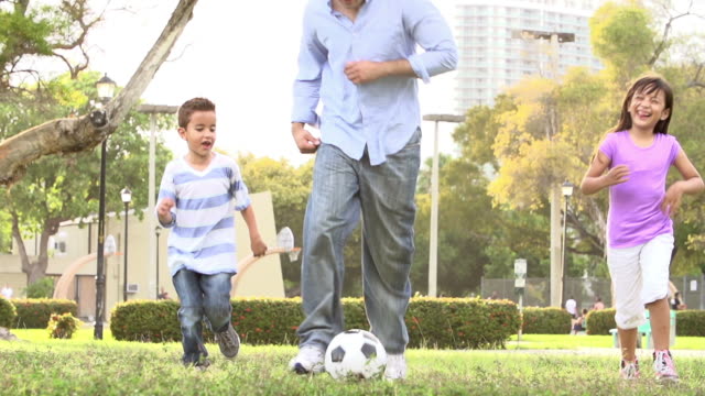 Vater-mit-Kindern-spielen-Fußball-im-Park-zusammen