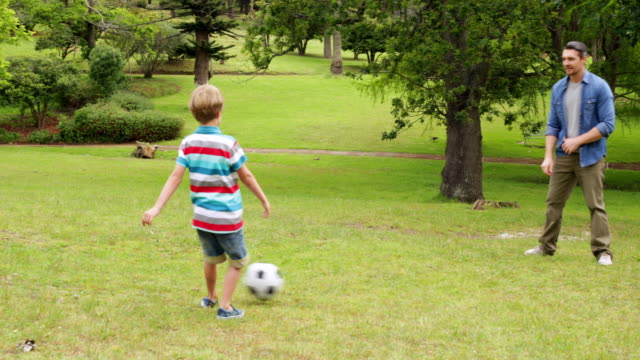 Father-and-son-kicking-football-back-and-forth-in-park