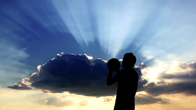 Silhouette-Mann-spielen-mit-einem-ball-auf-einem-Hintergrund-der-Wolken-bei-Sonnenuntergang