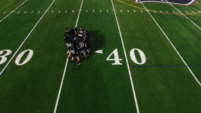 The-camera-spins-from-above-as-a-football-team-in-a-huddle-gets-hyped-and-runs-onto-the-field