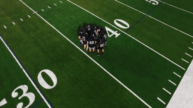 The-camera-spins-from-above-as-a-football-team-in-a-huddle-gets-hyped-before-a-game