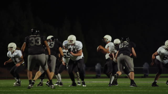 A-football-is-snapped-during-a-game-and-then-thrown-toward-the-camera-to-a-teammate-at-night