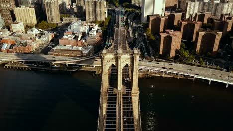 Top-aerial-view-of-the-Brooklyn-bridge-through-the-East-river-to-Manhattan-in-New-York,-America.-Flag-waving-on-the-wind