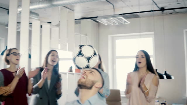 Glücklich-kaukasischen-Arbeitskraft-jonglieren-Fußball-im-Kopf.-Fröhliche-Mischlinge-Führungskräfte-feiern-Geschäftserfolg-im-Büro-4K