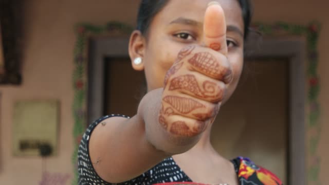 Mid-shot-of-young-beautiful-Indian-woman-points-thumbs-up-for-approval-liking-accept-good-sure-fun-joy-at-camera-with-her-henna-tattoo-hand-smiling-positive-confident-leader-conviction-static-shot
