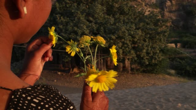 Indische-Teenager-schöne-Mädchen-mit-Blumen-gelb-warten-auf-einer-Anhöhe-unter-einem-Baum-an-einem-Sommertag-in-der-Liebe-glücklich-Freude-Sonne-tropischen-heißen-hellen-Sonnenschein-Inhalt-Blick-in-die-Kamera-handheld-stabilisiert