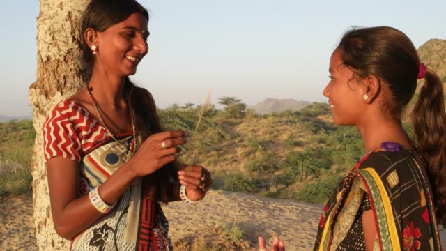 Two-girls-sharing-secrets-and-joking-kidding-fun-gossip-outdoor-tree-park-public-alone-secrets-hidden-casual-friends-buddy-sari-India-Rajasthan