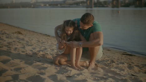 Niño-y-padre-buscando-conchas-en-la-arena-de-playa