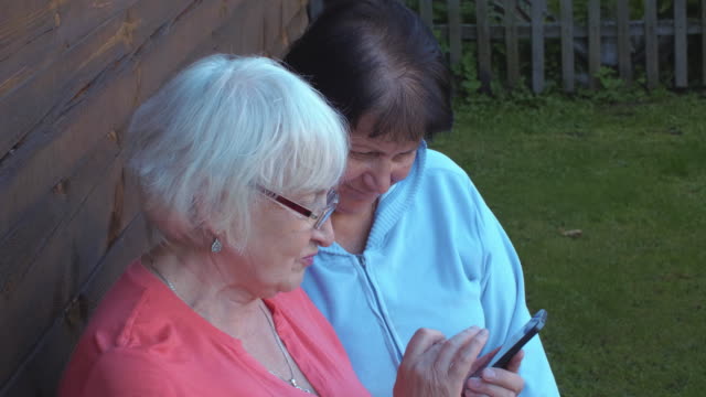 Two-elderly-woman-browsing-mobile-phone-together-in-countryside-garden