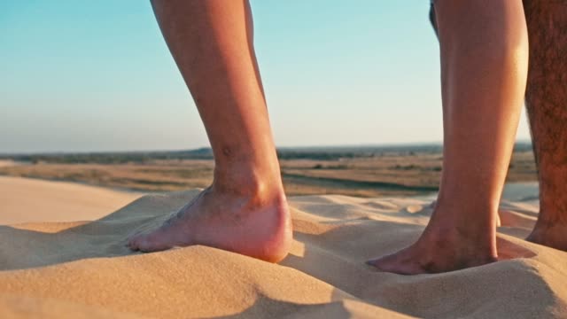 Nahaufnahme-der-Beine-einer-jungen-Frau-und-Mann-genießen-den-Sonnenuntergang-auf-dem-Gipfel-eines-einsamen-Sanddüne