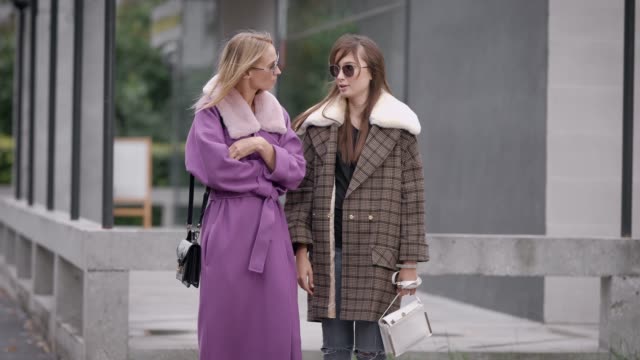 zwei-trendige-und-modische-Frauen-tragen-Mäntel-auf-Stadtstraße-stehen-und-miteinander-zu-reden
