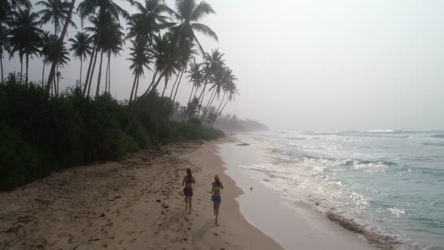 Zwei-gesunde-Lebensweise-junge-Frauen-Freunde-laufen-am-tropischen-Strand-bei-Sonnenaufgang-am-Morgen,-Luftbild-Drohne-anzeigen-Filmmaterial