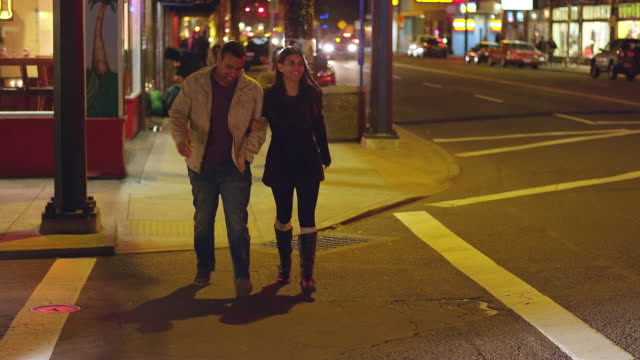A-young-couple-walking-downtown-at-night