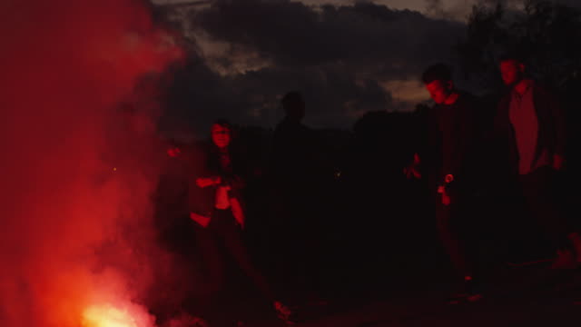 Group-of-Teenagers-Hanging-Out-and-Dancing-in-Light-of-Red-Signal-Flare-Outdoors.