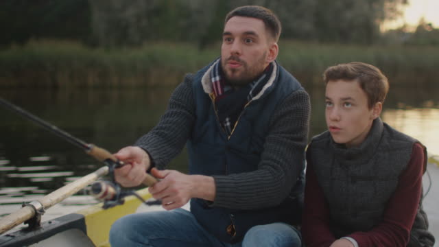 Father-and-Son-Sitting-in-the-Boat-Fishing.-Father-Swings-Fishing-Rod.