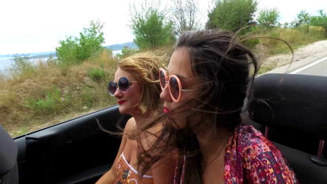 Zwei-unbeschwerte-Mädchen-feiern-während-der-Fahrt-im-cabriolet