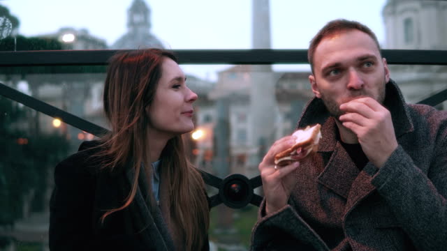 Young-attractive-couple-have-a-break-in-city-centre.-Man-and-woman-sitting-in-the-evening-outdoors,-eating-sandwiches