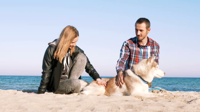 Joven-pareja-caucásica-en-la-playa-con-perro-husky-siberiano