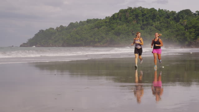 Slow-motion-shot-of-two-women-running-on-beach.