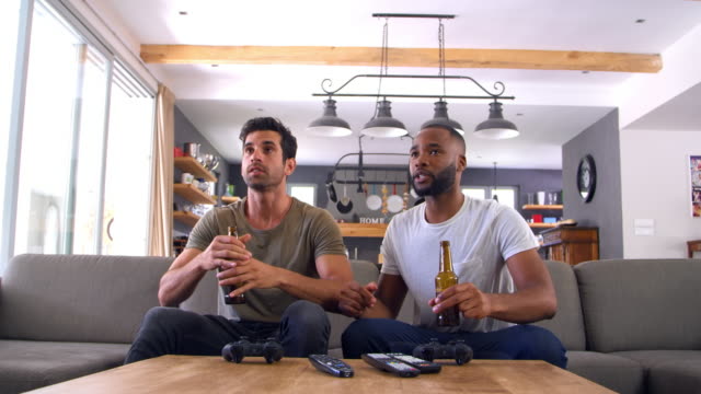 Zwei-männliche-Freunde-sitzen-auf-Sofa-und-Uhr-Sport-im-Fernsehen