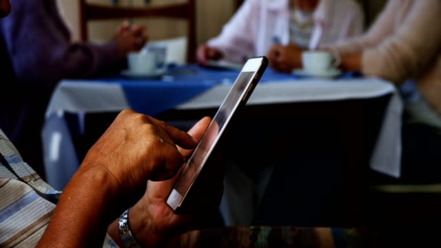 Senior-woman-mit-digital-Tablette-mit-seinen-Freunden-sitzt-im-Hintergrund-4k