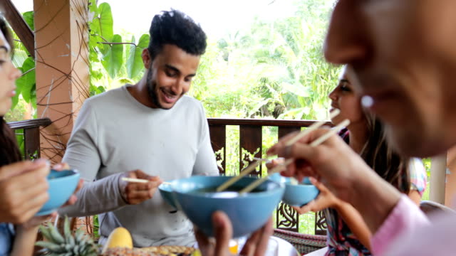 Personas-alimentadas-mutuamente-con-deliciosos-fideos-asiáticos-alimentos,-grupo-de-amigos-sentarse-en-la-mesa-en-terraza-vista-en-Bosque-Tropical