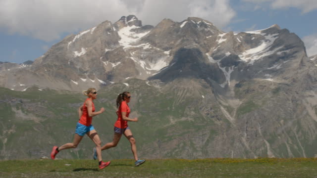 Zwei-Frauen-laufen-in-Zeitlupe-in-Bergen-zu-sprechen-und-Lächeln.