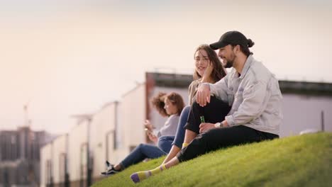 Attraktive-junge-Leute-sitzen-auf-einer-grünen-Wiese-und-genießen-Sommer-in-der-Stadt