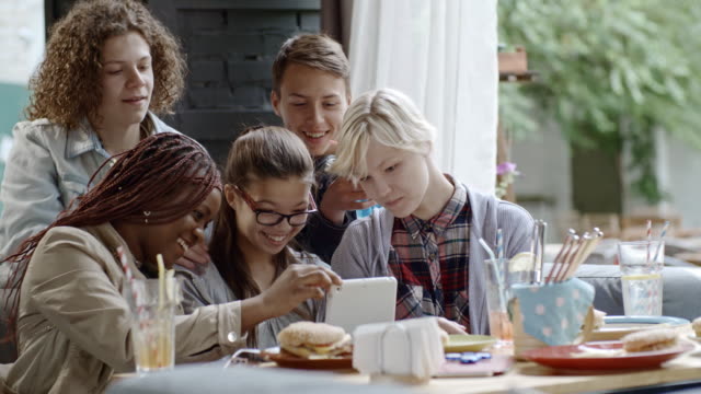 Compañía-de-adolescentes-con-tableta-Digital-en-el-café-al-aire-libre