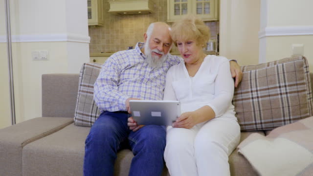 Ältere-Frau-und-senior-Mann-nutzt-Tablet-entspannend-am-Sofa-zu-Hause
