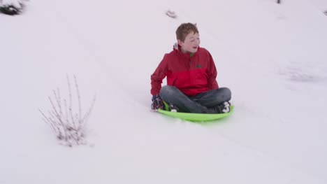 Boy-sledding-abajo-colina-cubierta-de-nieve-en-invierno